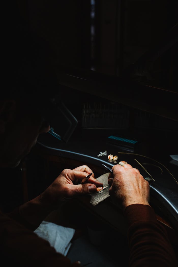 Close-up of an artisan crafting jewelry in a dimly lit Sardegna workshop.