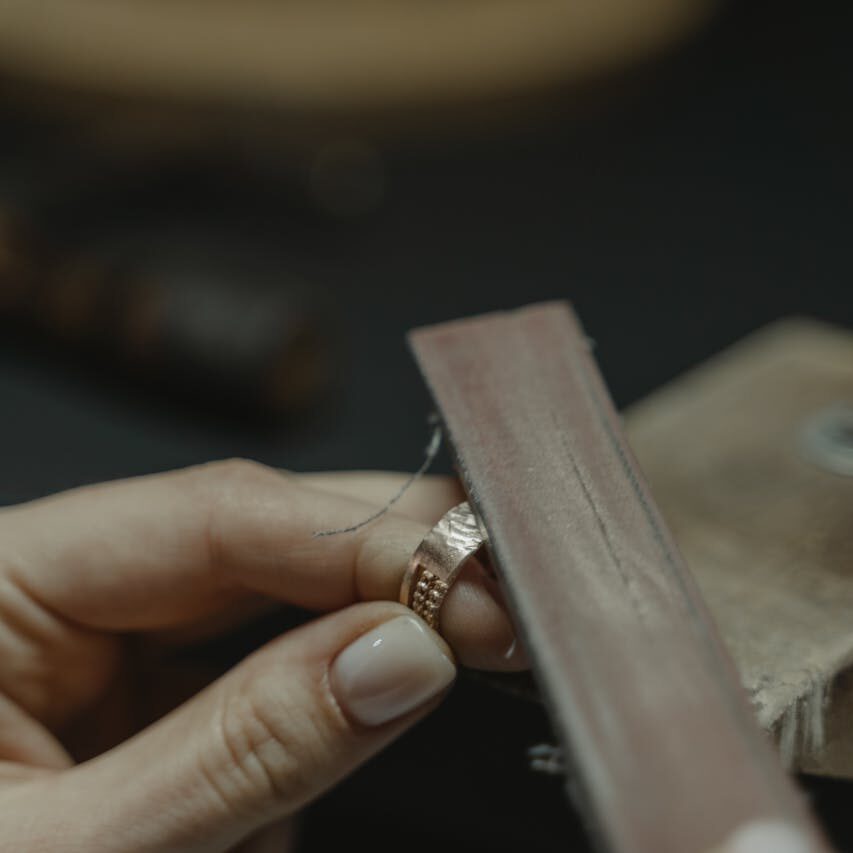 Close-up of a craftsman polishing a gold ring using a tool, showcasing fine jewelry making.